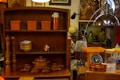 A cozy vintage kitchen setting with a wooden shelf that holds orange storage containers, a series of stacked bowls, a copper clock, a brown teapot, and smaller matching cups. Next to it, there are wooden pepper mills and a metal dome pendant light. An orange kitchen scale and assorted jars sit on the counter. In the background, there are various decorative items such as a globe, artwork, and vases.