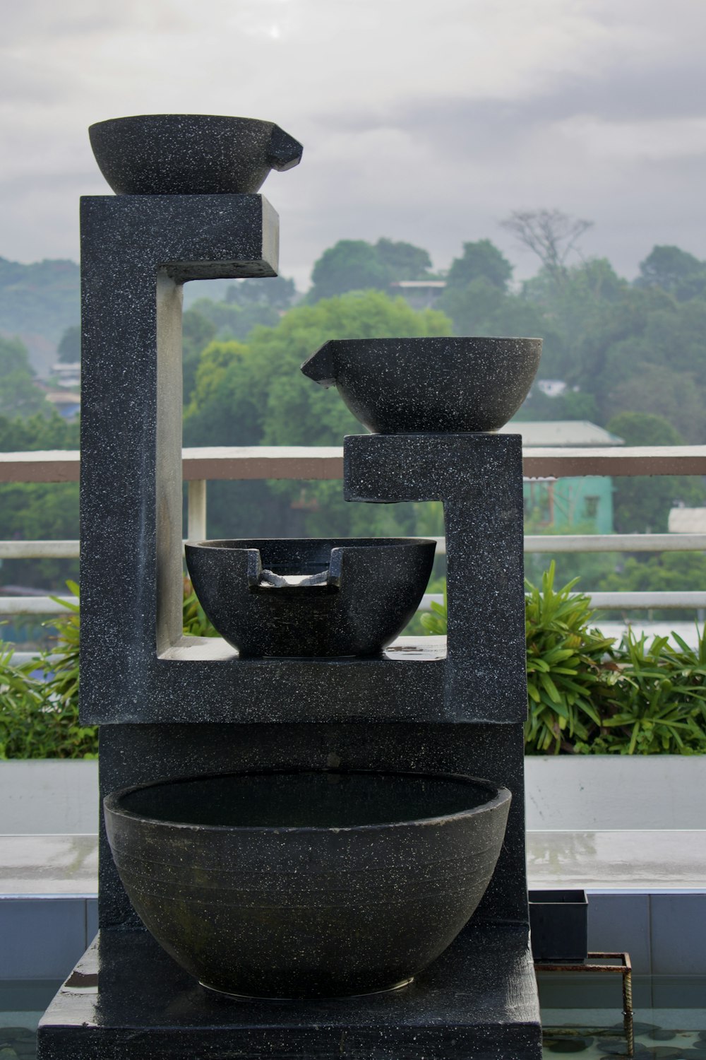 a couple of black pots on a window sill with trees and a cloudy sky