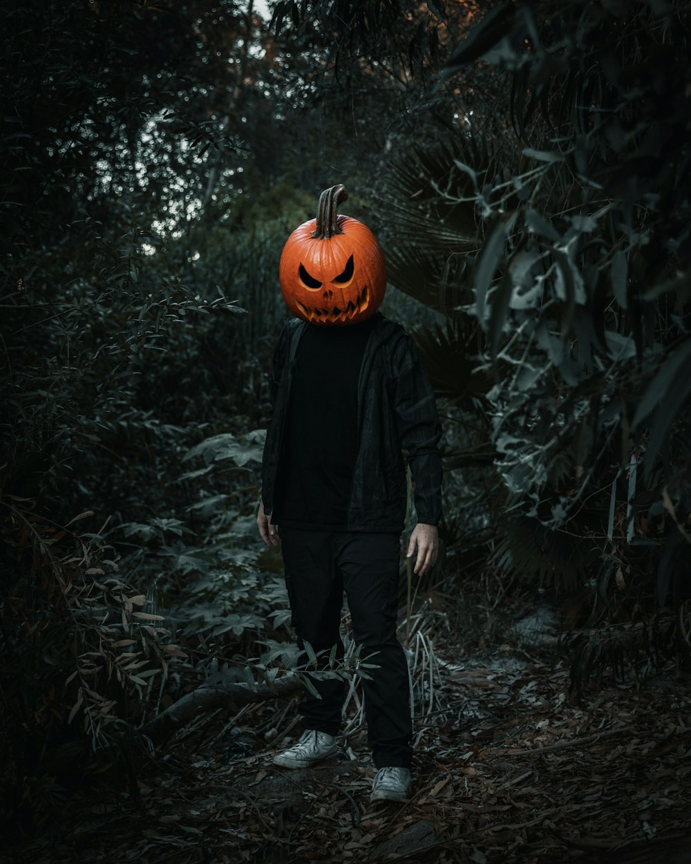 a person standing next to a carved pumpkin in a forest
