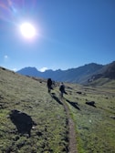 A group of hikers walking along a mountain trail under clear skies.