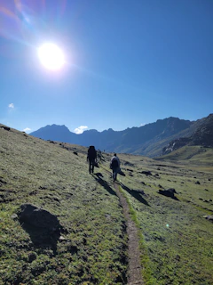 A group of travelers hiking along a rugged mountain trail under a bright blue sky.