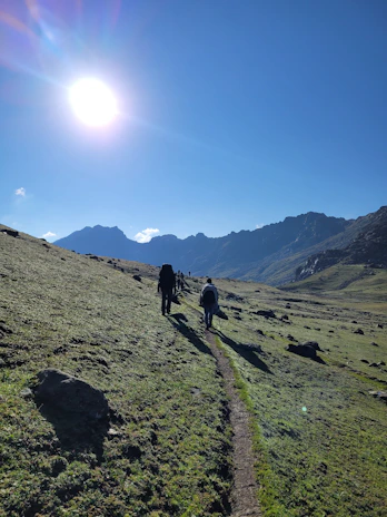 A group of travelers hiking along a rugged mountain trail under a bright blue sky.