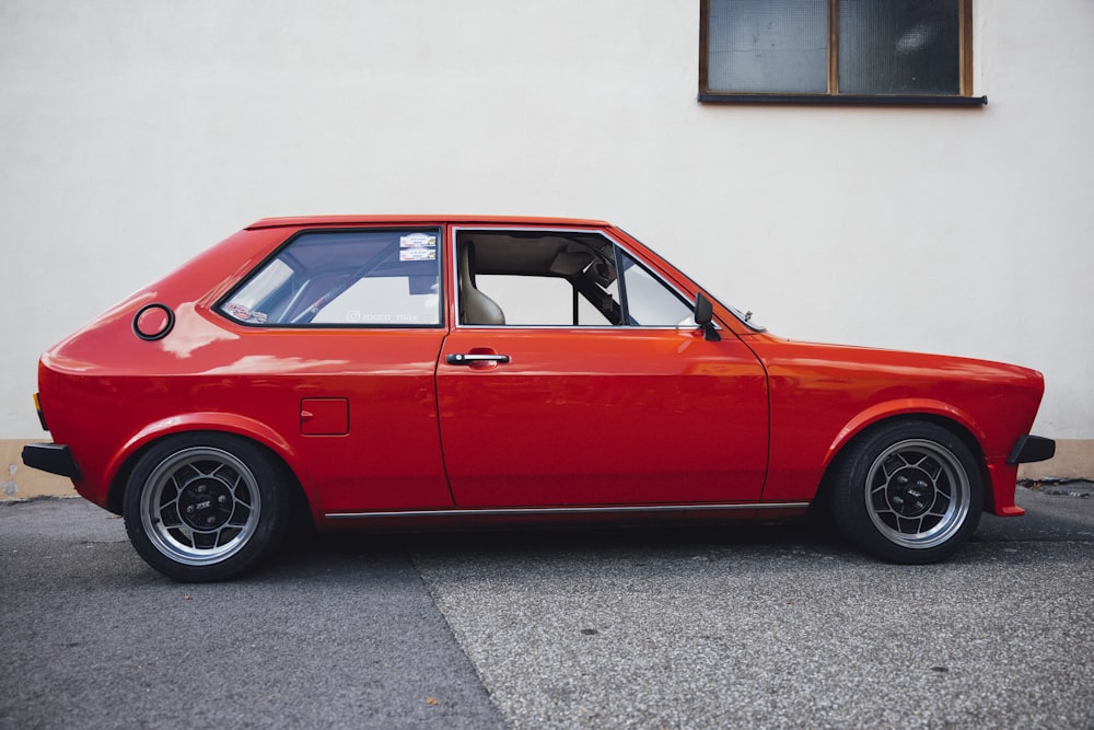 a red car parked in front of a white wall