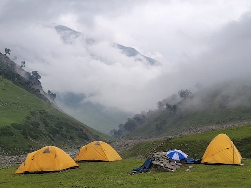 a group of tents on a grassy hill with clouds in the background