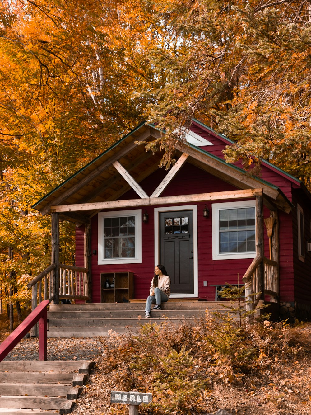 a person sitting on a porch of a red house with yellow leaves
