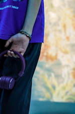 Close-up of hands holding a music player with headphones and gentle purple and pink hues in the background.