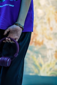 Close-up of hands holding a music player with headphones and gentle purple and pink hues in the background.