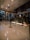 A modern hotel reception area featuring a sleek design. The counter is equipped with digital displays and several computers. The ambient lighting is warm, with pendant lights hanging from the ceiling. Decorative ropes guide visitors along the polished, reflective floor. There is a potted orchid on the counter, adding a touch of elegance.
