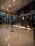 A modern hotel reception area featuring a sleek design. The counter is equipped with digital displays and several computers. The ambient lighting is warm, with pendant lights hanging from the ceiling. Decorative ropes guide visitors along the polished, reflective floor. There is a potted orchid on the counter, adding a touch of elegance.