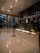A modern hotel reception area featuring a sleek design. The counter is equipped with digital displays and several computers. The ambient lighting is warm, with pendant lights hanging from the ceiling. Decorative ropes guide visitors along the polished, reflective floor. There is a potted orchid on the counter, adding a touch of elegance.