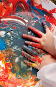 Close-up of hands covered in bright paint mixing freely on a canvas full of wild colors.