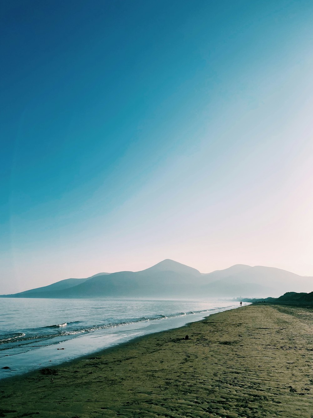 a beach with a body of water and mountains in the background