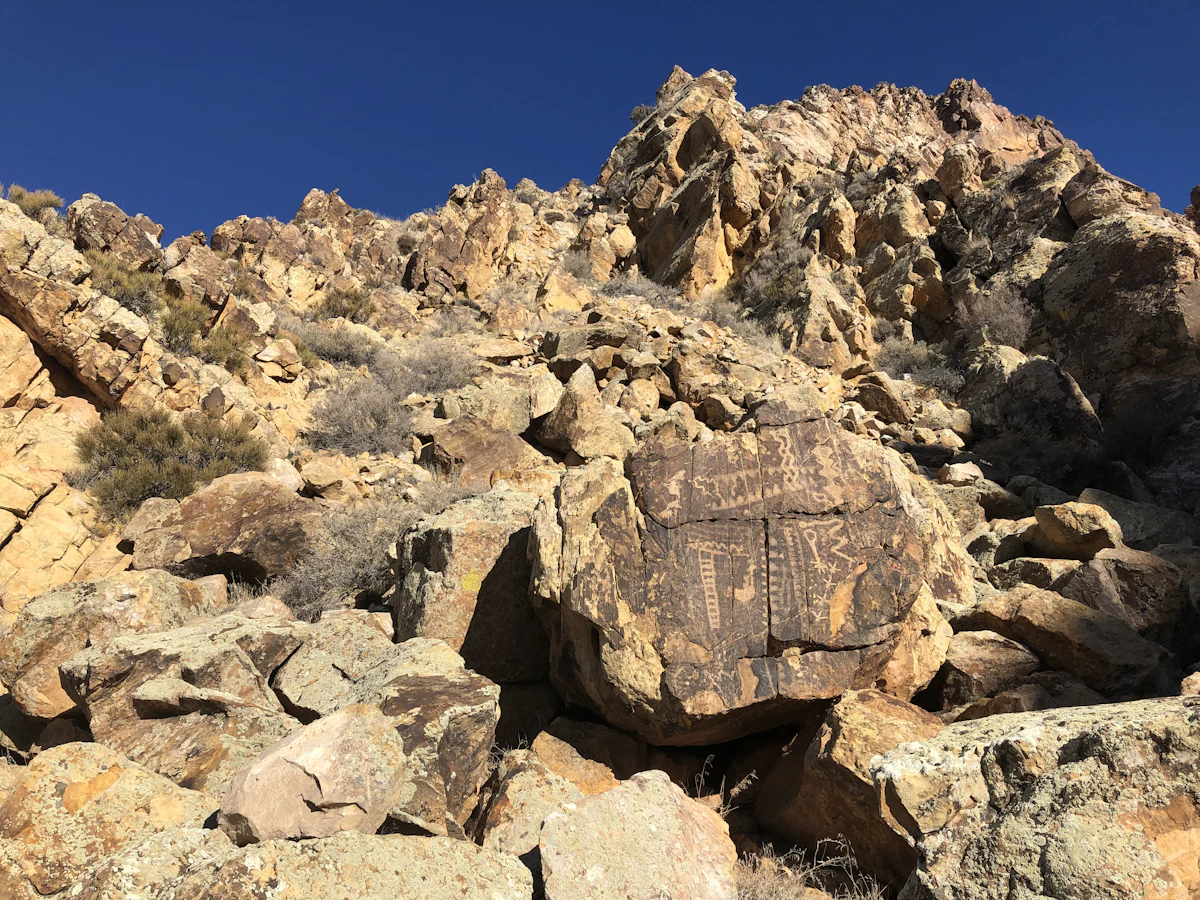 A boulder carved with petroglyphs on a rocky slope at Parowan Gap, under a deep blue sky