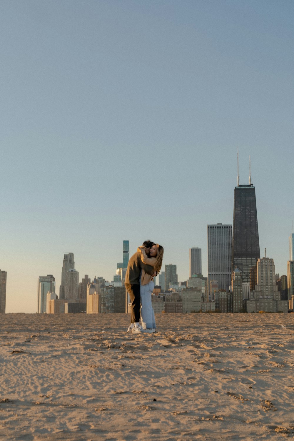 a man and woman kissing on a beach with a city in the background
