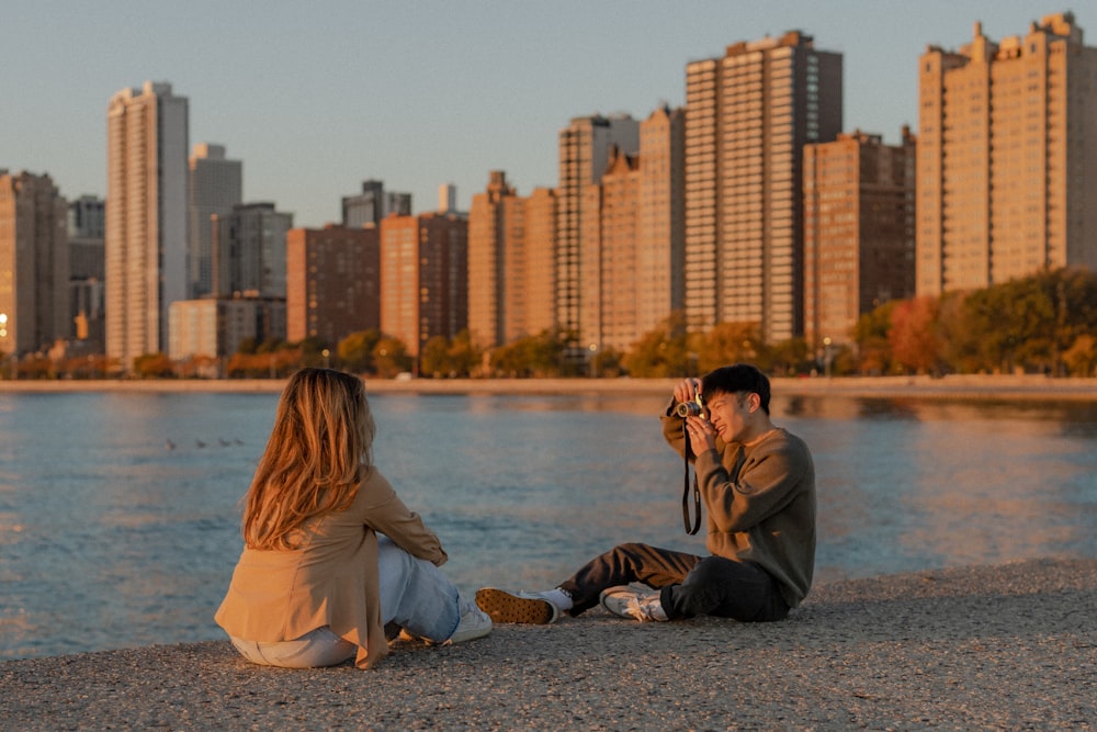 a man and woman sitting on a rock by a body of water