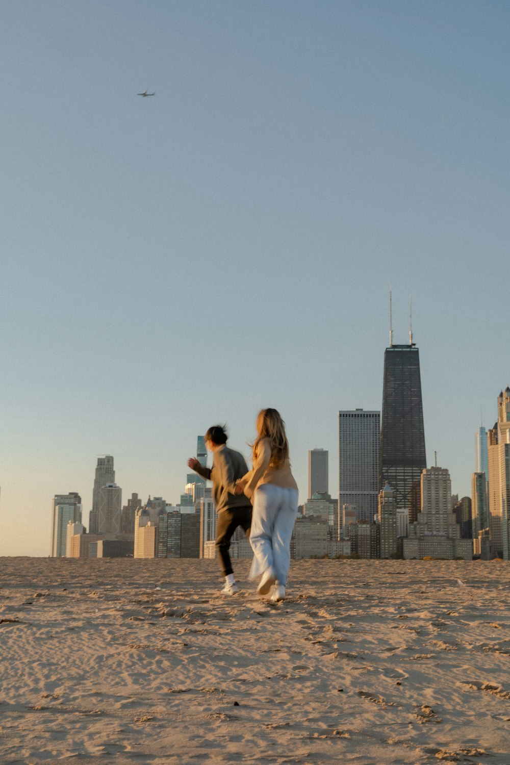 a man and woman holding hands on a beach with a city skyline in the background