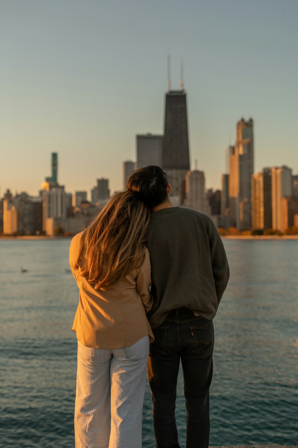 a man and woman kissing in front of a body of water with a city in the background