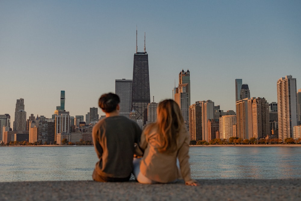 Un hombre y una mujer sentados en una repisa con vistas al horizonte de una ciudad