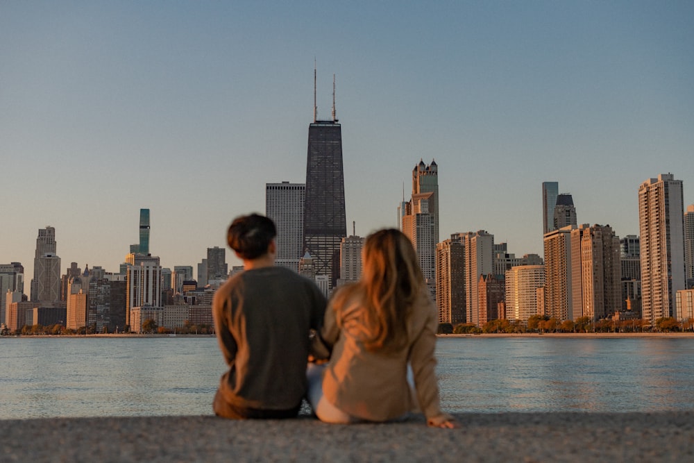 a man and woman sitting on a ledge overlooking a city skyline