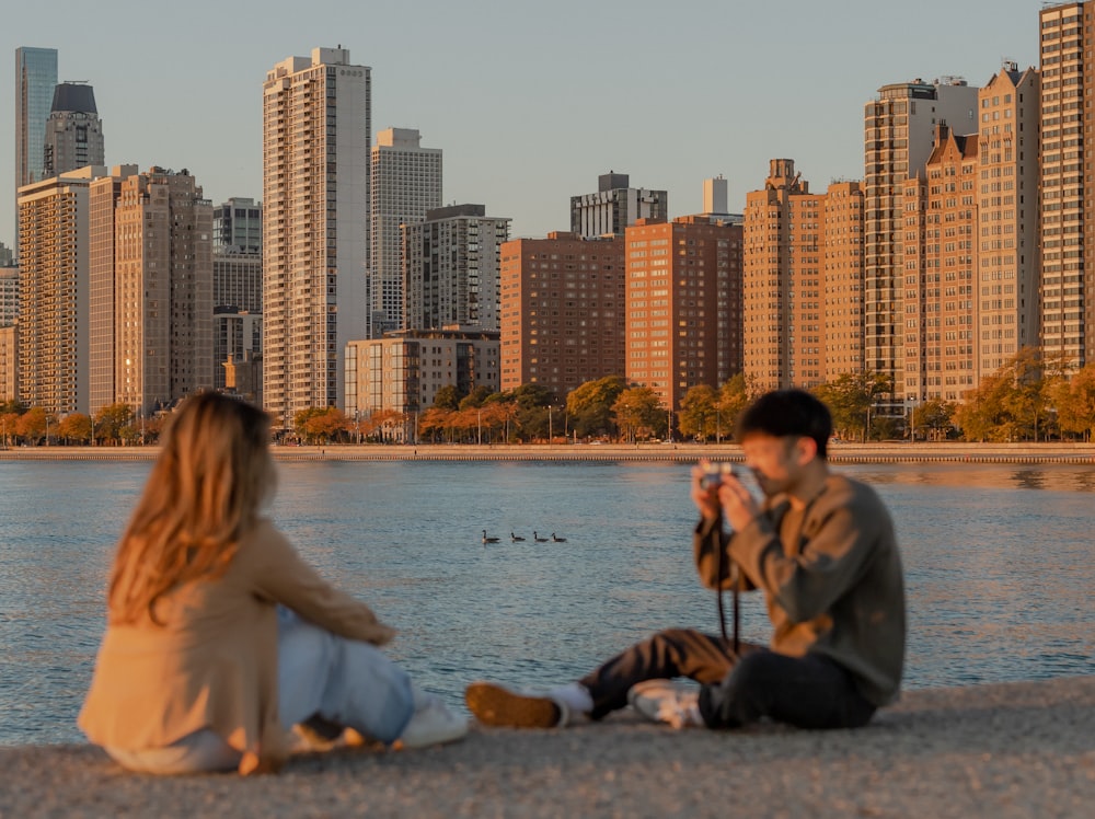 a man and woman sitting on a beach with a city skyline in the background
