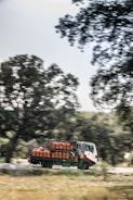 A truck is carrying several gas cylinders, driving along a road bordered by trees. The background is slightly blurred, indicating motion.