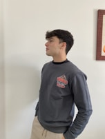 Model wearing a grey dark sweatshirt with clean lines, standing against a muted urban wall.
