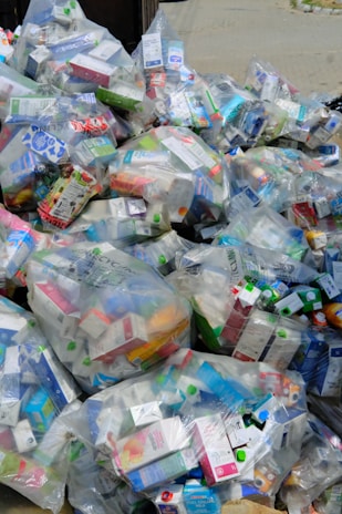 A large pile of household waste, primarily consisting of plastic bags filled with various types of cartons and bottles. The waste is organized in transparent bags with visible branding and labels.