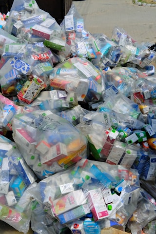 A large pile of household waste, primarily consisting of plastic bags filled with various types of cartons and bottles. The waste is organized in transparent bags with visible branding and labels.