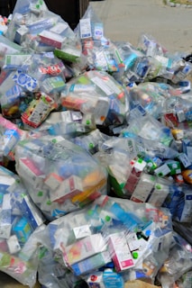 A large pile of household waste, primarily consisting of plastic bags filled with various types of cartons and bottles. The waste is organized in transparent bags with visible branding and labels.