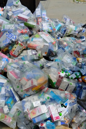 A large pile of household waste, primarily consisting of plastic bags filled with various types of cartons and bottles. The waste is organized in transparent bags with visible branding and labels.