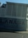 A building facade featuring a large sign with the text 'LANASA Produce Inc.' and a phone number beneath it. The structure is a combination of dark and light shades, with a slanted sidewalk in front. The overall scene is under a clear blue sky with no visible people.