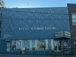 A brick building with a large sign reading 'WRF & S N Plumbing & Heating' on the front facade. There are advertisements for Goulds Pumps, water conditioners, and supplies on the wall. The storefront features large glass windows displaying plumbing-related items. The door on the left is labeled '15 N Main' and there is a sign indicating propane cylinder refills.