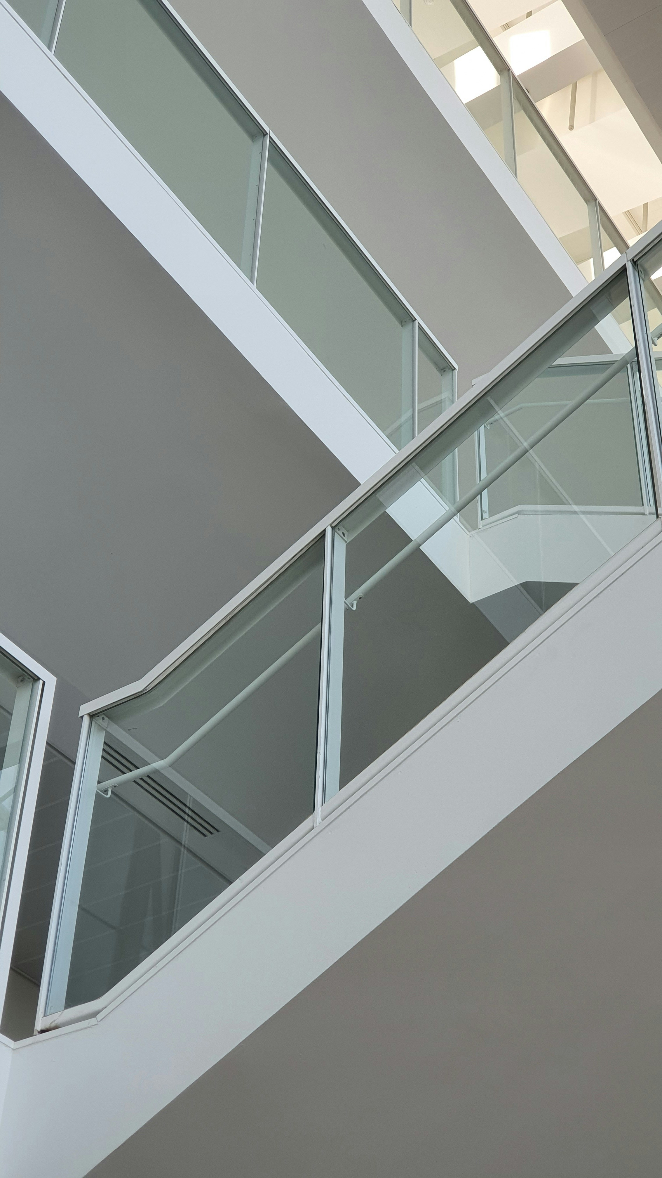 Modern glass stair railing on white staircase with natural light streaming through floor-to-ceiling windows