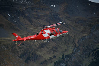 a red and white helicopter flying over a mountain