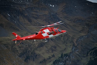 a red and white helicopter flying over a mountain
