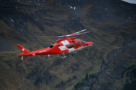 a red and white helicopter flying over a mountain
