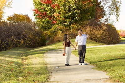 A couple holding hands, walking along a vibrant autumn path.