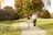 Outdoor photo of a happy couple walking hand in hand through a sunlit park in autumn.
