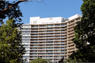 A modern apartment building under clear blue sky with balconies and greenery around.