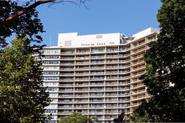 A modern apartment building under clear blue sky with balconies and greenery around.