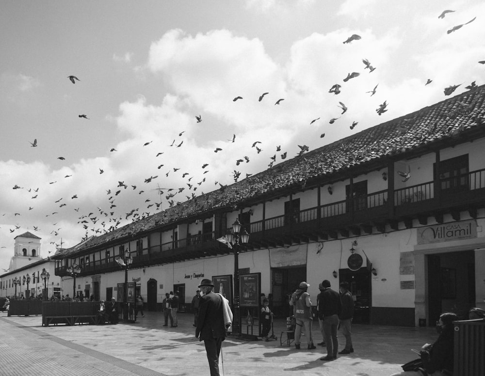 a group of people outside of a building with birds flying around