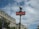 A classic Parisian metro sign with a red background and white lettering is prominently displayed. The sign is attached to a vintage-style green pole topped with a spherical light. In the background, ornate Haussmann-style buildings with mansard roofs and dormer windows are visible under a partly cloudy sky.