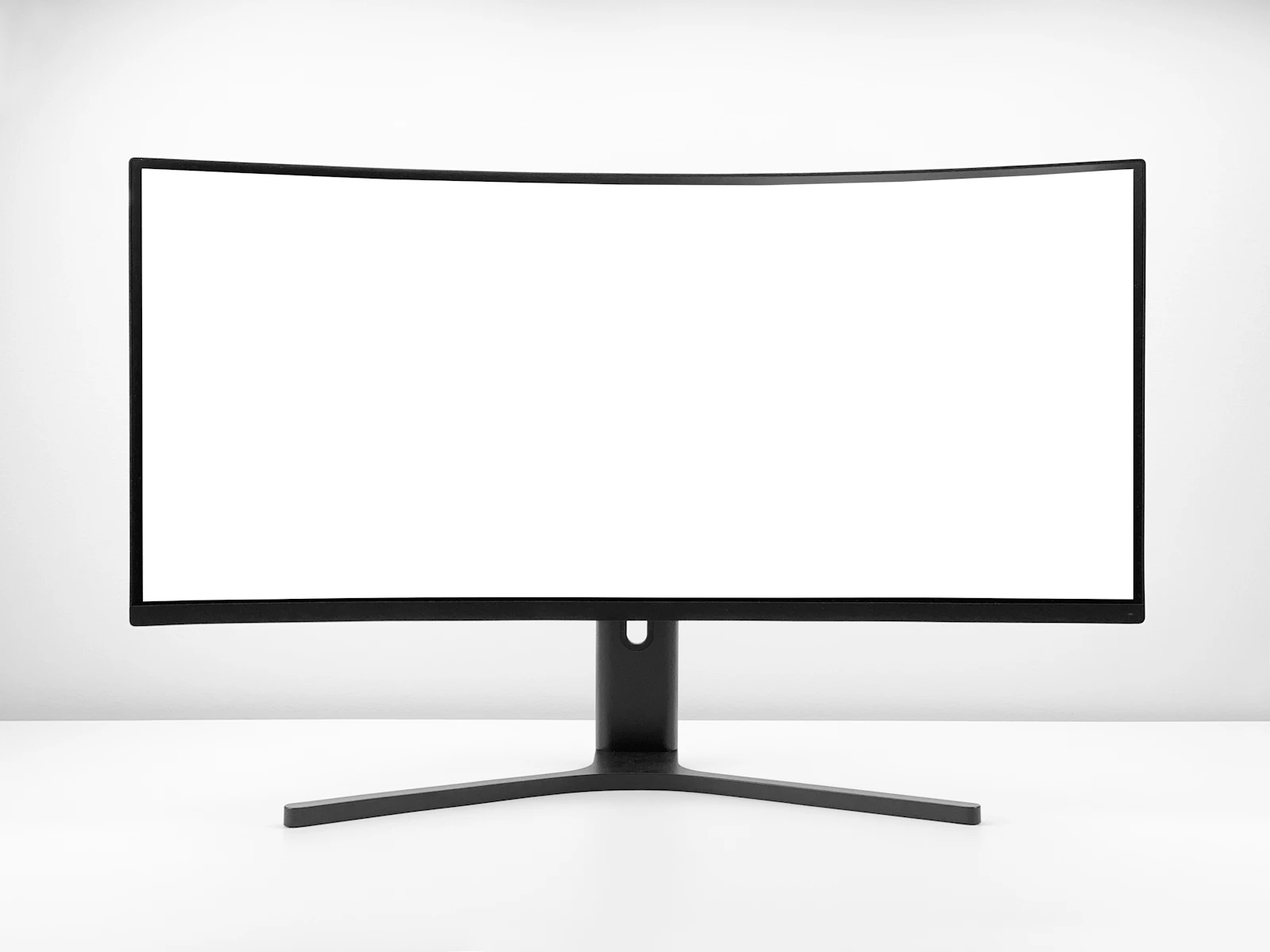A large curved widescreen computer monitor with a blank white display, mounted on a black stand against a plain light gray studio background, evoking a clean home office desk setup.