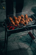 A grill with multiple pieces of marinated meat cooking over red-hot coals. The chicken is placed on a metal grate, and the glowing embers illuminate the scene, casting a warm glow.