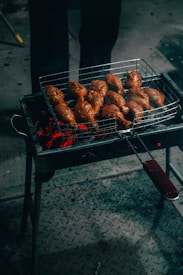 A grill with multiple pieces of marinated meat cooking over red-hot coals. The chicken is placed on a metal grate, and the glowing embers illuminate the scene, casting a warm glow.