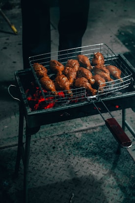 A grill with multiple pieces of marinated meat cooking over red-hot coals. The chicken is placed on a metal grate, and the glowing embers illuminate the scene, casting a warm glow.
