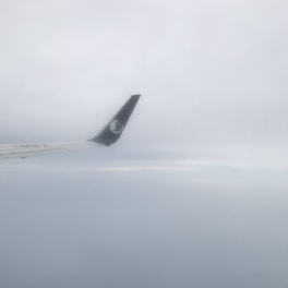 An airplane wingtip is visible against a backdrop of cloudy skies. The sky appears overcast, with varying shades of grey and white.