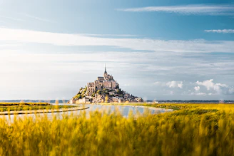 a castle on a hill by a body of water with Mont Saint-Michel in the background