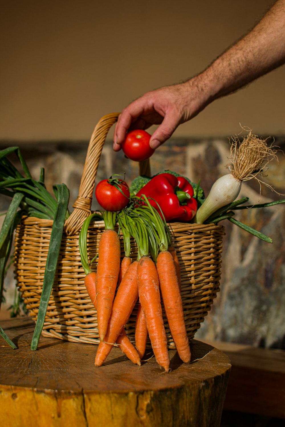 uma mão segurando uma cenoura sobre uma cesta de legumes