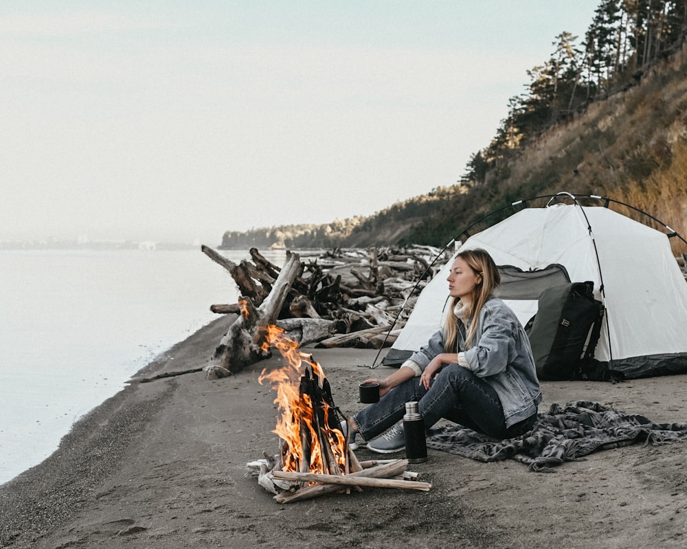 a man sitting next to a campfire on a beach